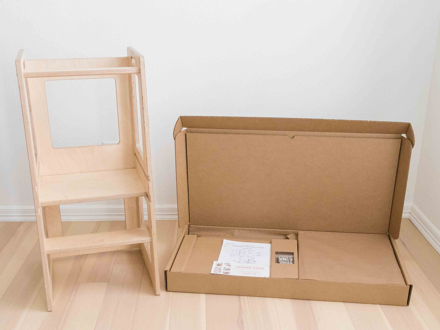 Toddler tower next to the eco friendly packaging it is shipped in. Showing the high quality of the tower and its packaging.