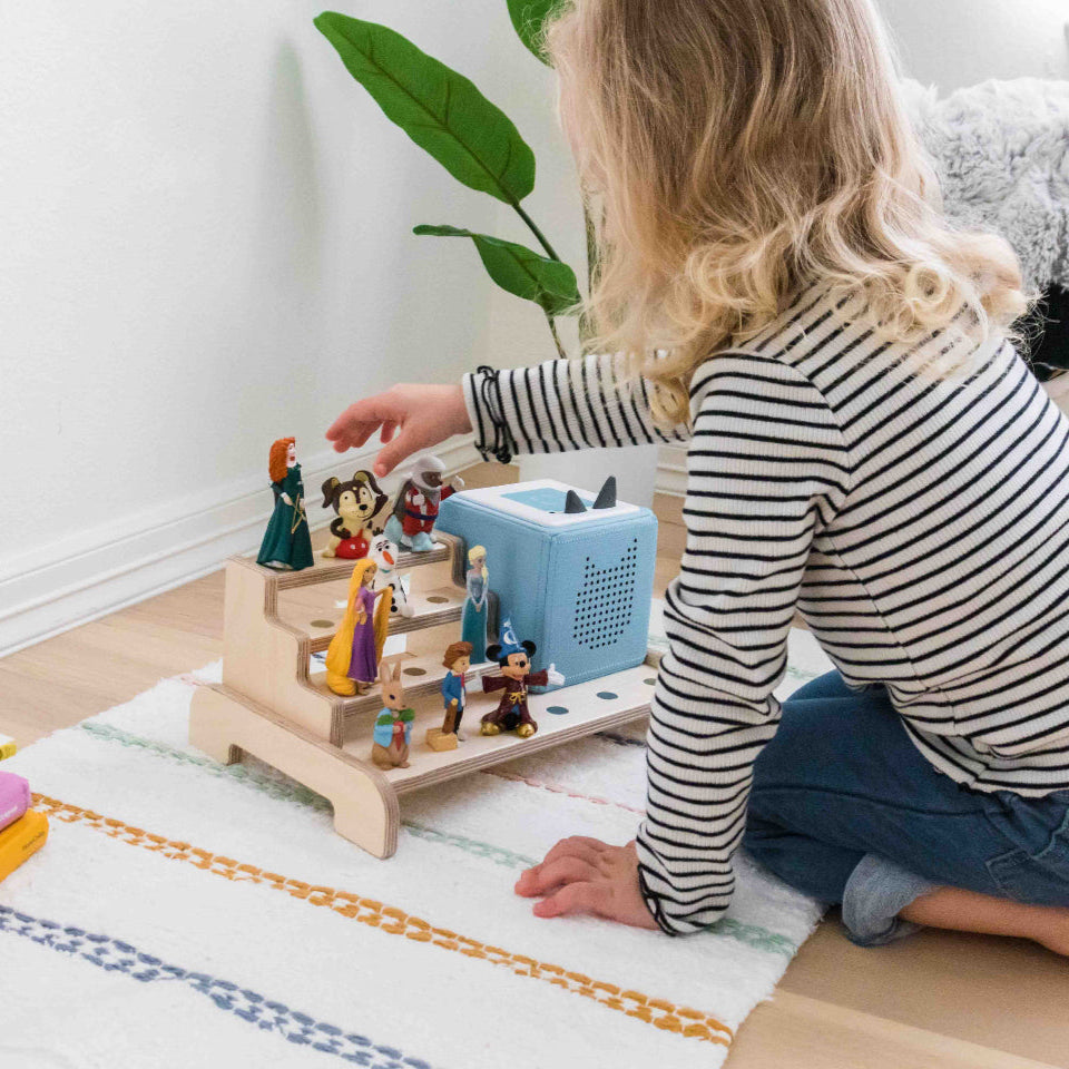A young girl playing with her toniebox that is placed on a wooden display designed to showcase a toniebox and tonie figures.