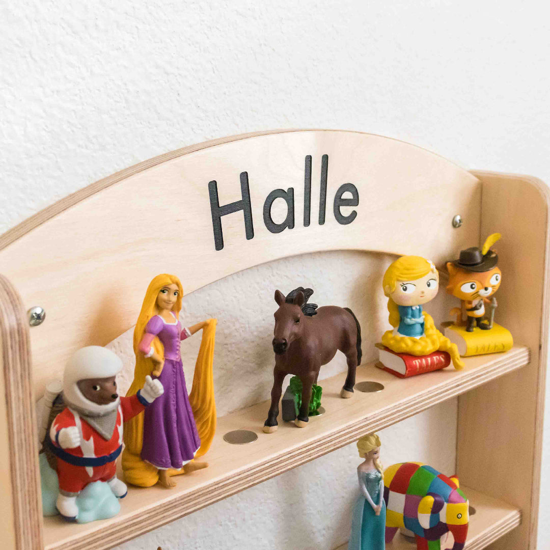 Close up of a wooden tonie shelf with a personalized name carved into the top of it. The names painted in with the color black.