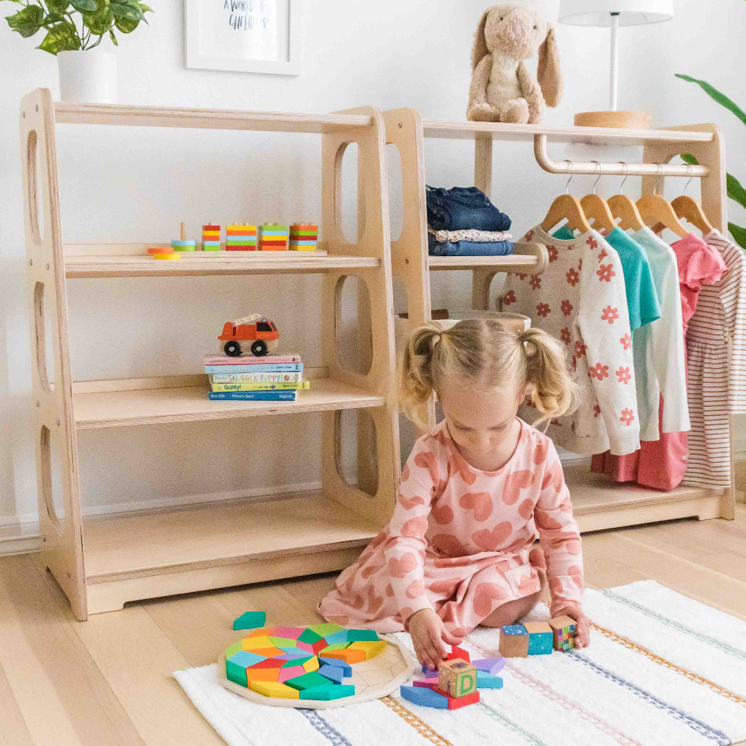 A you girl playing with blocks she grabbed from a wardrobe and to shelf set behind her.