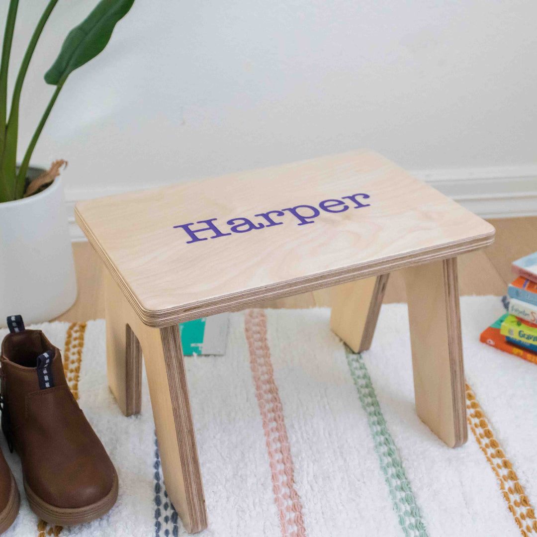 Kids Stool with a name carved into the top with the font Typewriter. The carved name is painted in with the color purple.