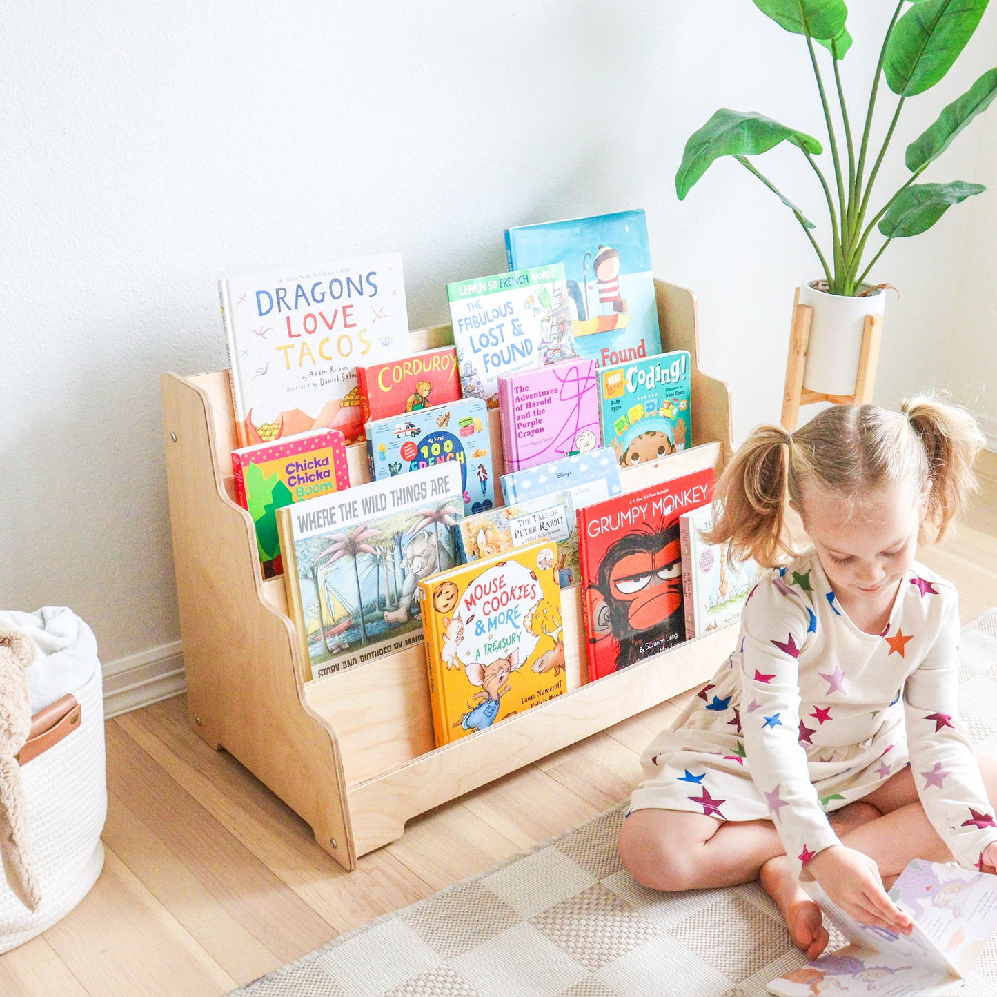 Child reading a book next to a wooden bookshelf filled with children's books in a bright room.
