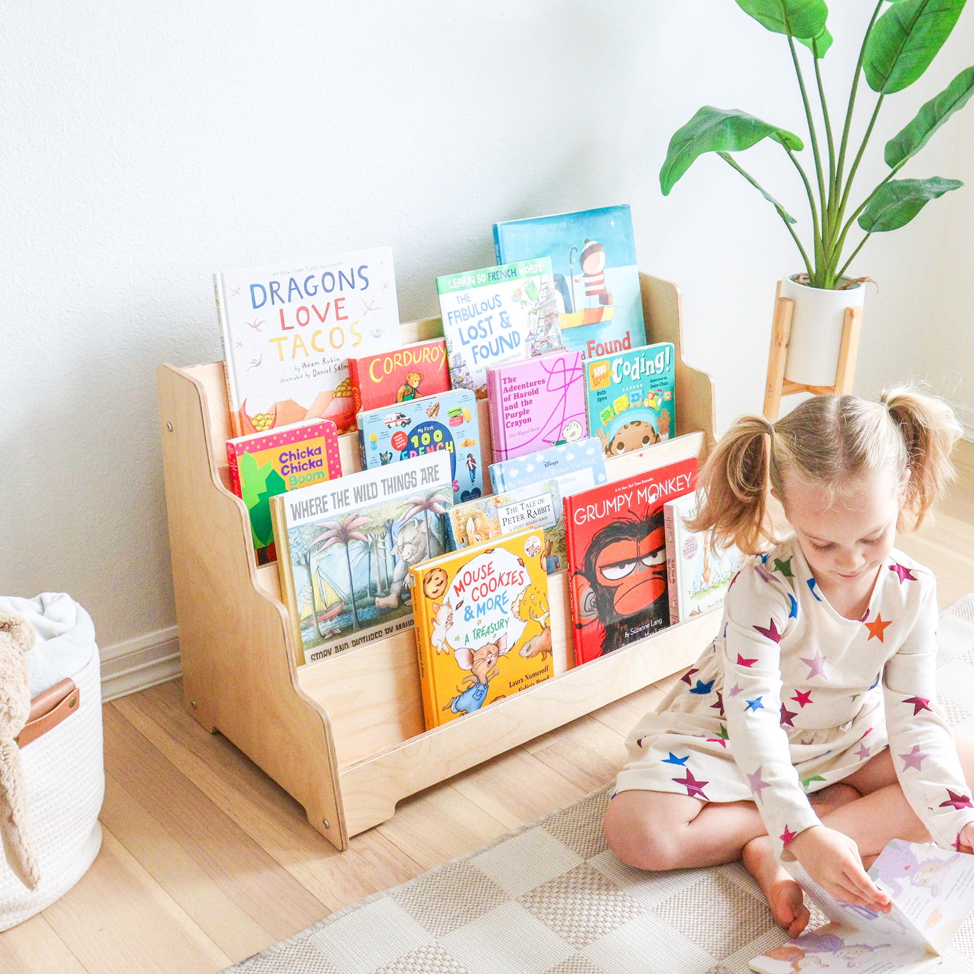Child reading a book next to a wooden bookshelf filled with children's books in a bright room.