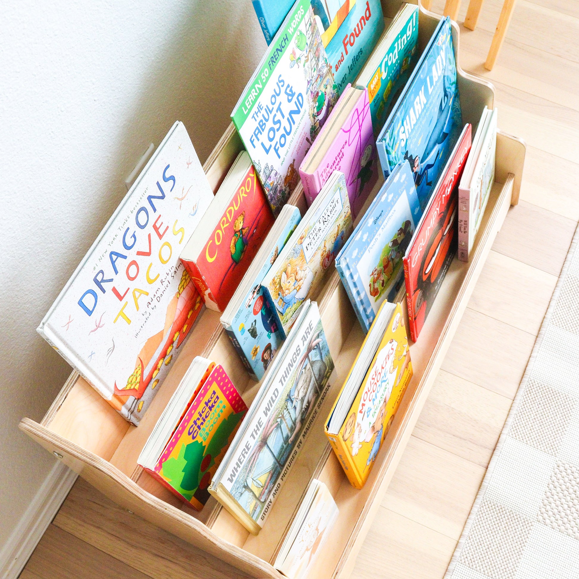 Open drawer filled with colorful children's books on a light wooden floor.