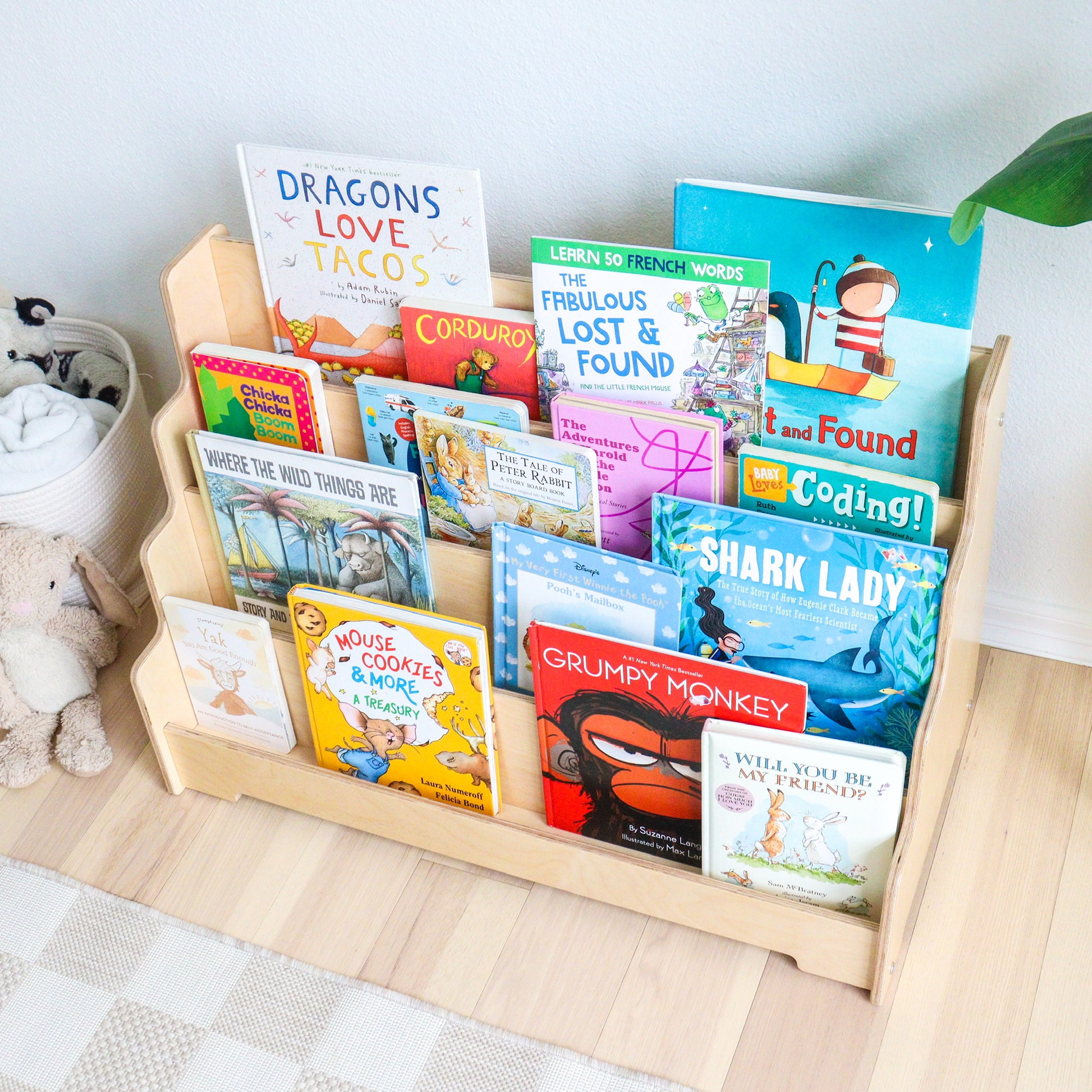 Children's books on a wooden bookshelf with a white wall background