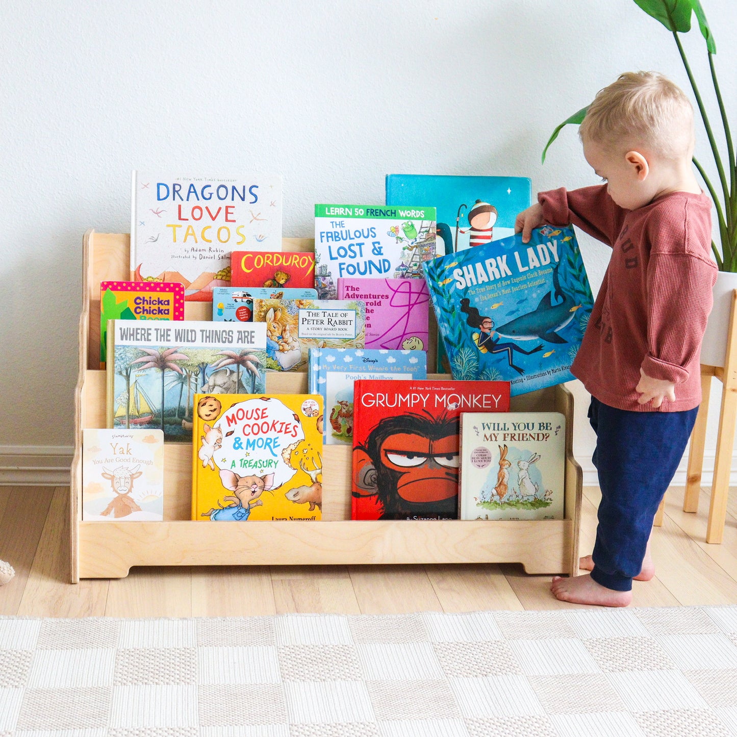 Child interacting with books on a wooden bookshelf in a room.
