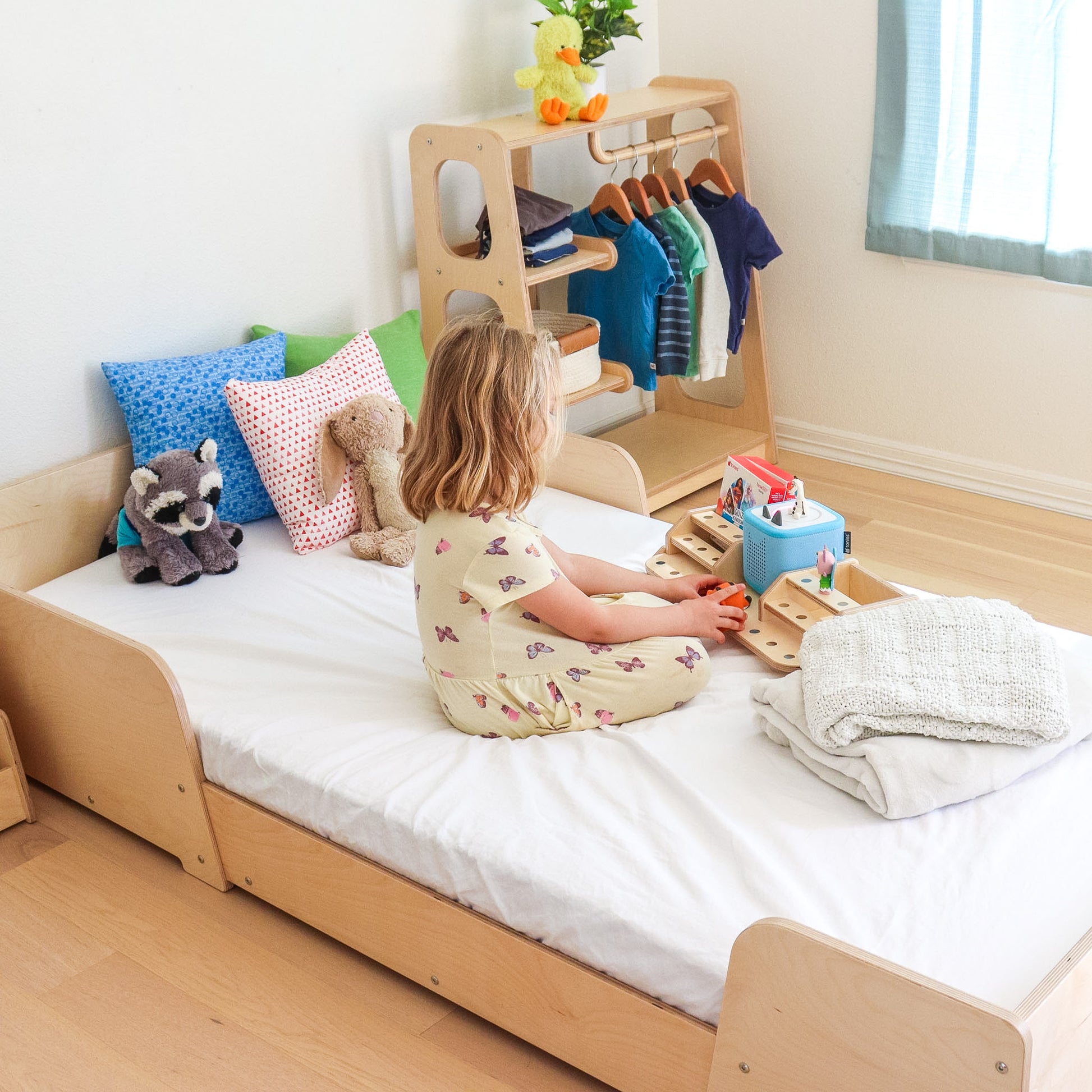 Young girl playing with a Toniebox on a Montessori inspired floor bed. 
