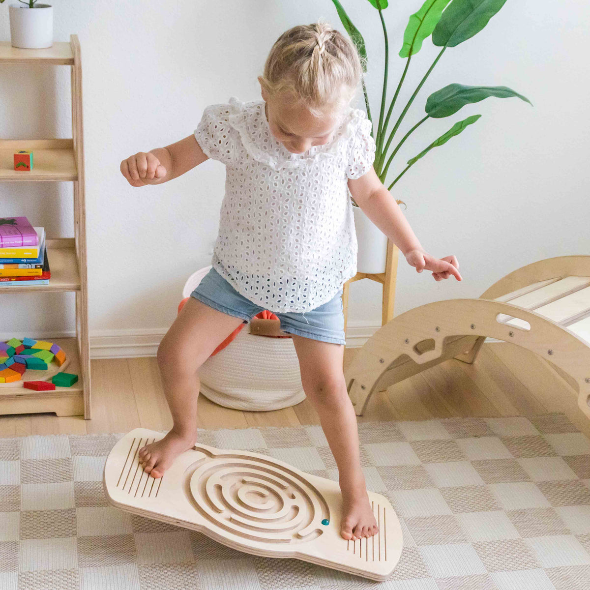 A girl balancing on a wooden maze balance board with a climbing arch behind her