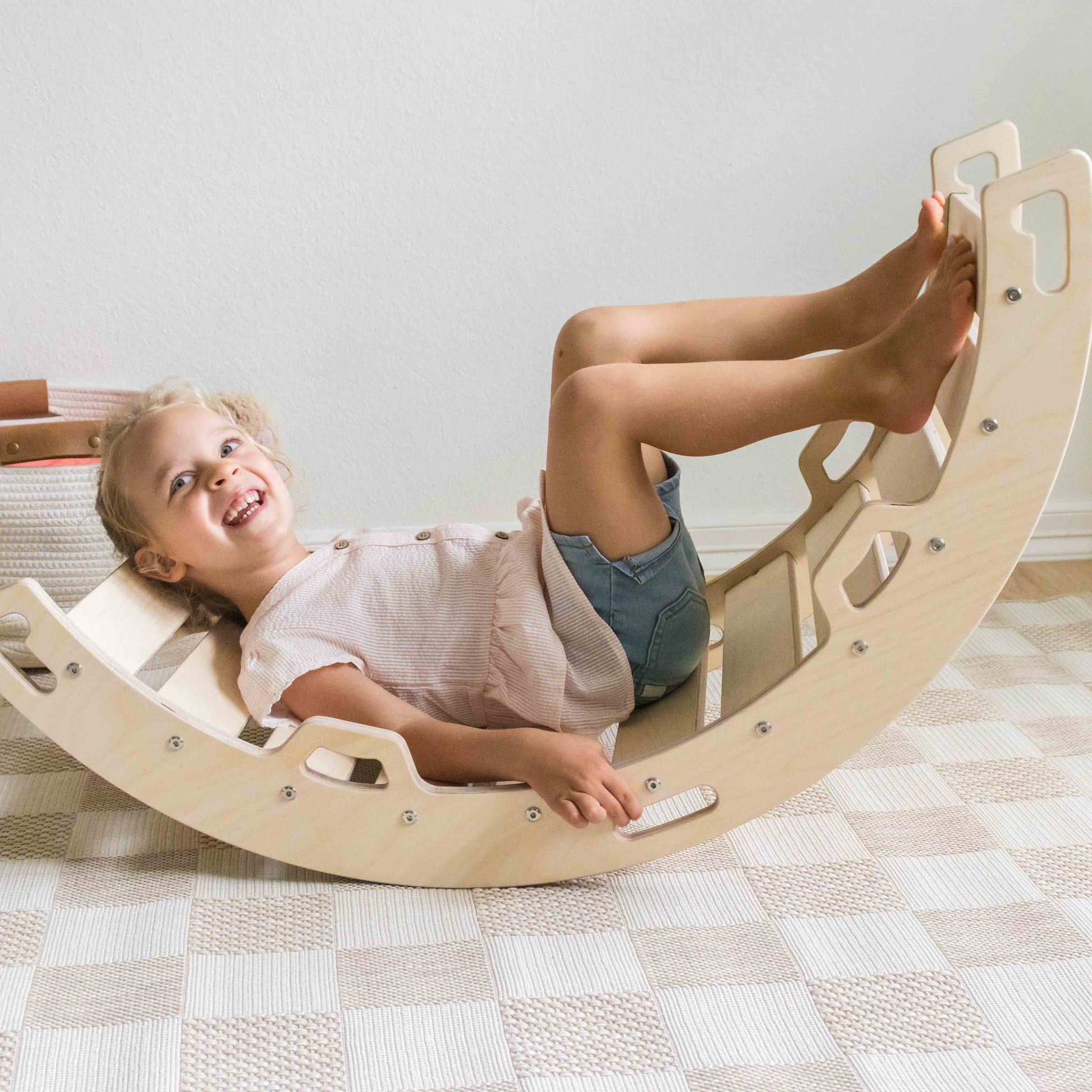 Child laughing while using a wooden rocking arch in a home setting