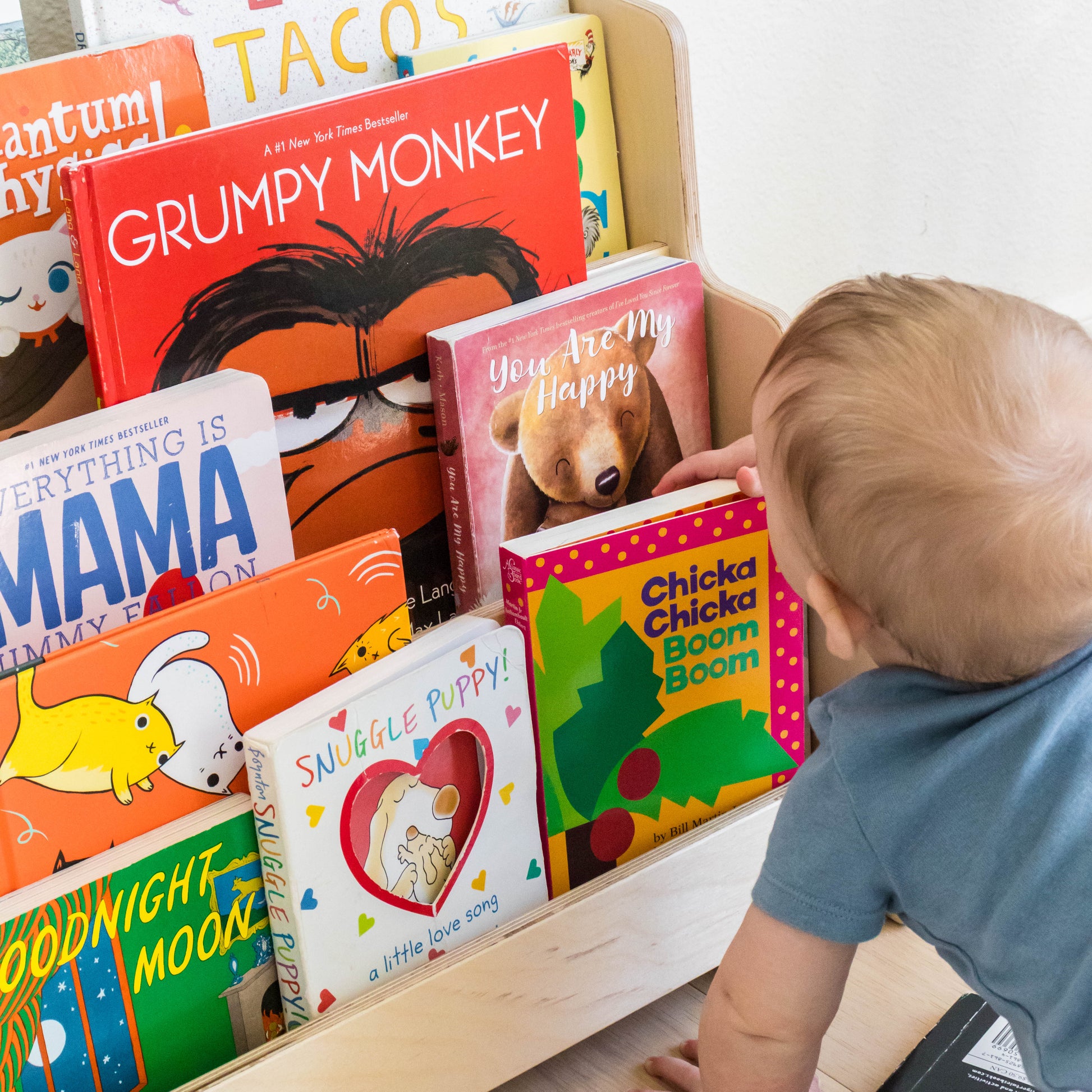 A child choosing a book to read from a front facing childrens bookshelf. 