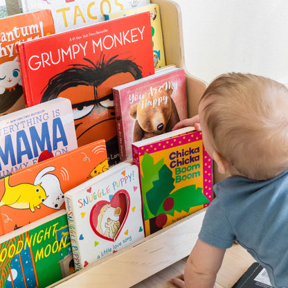 A child choosing a book to read from a front facing childrens bookshelf. 