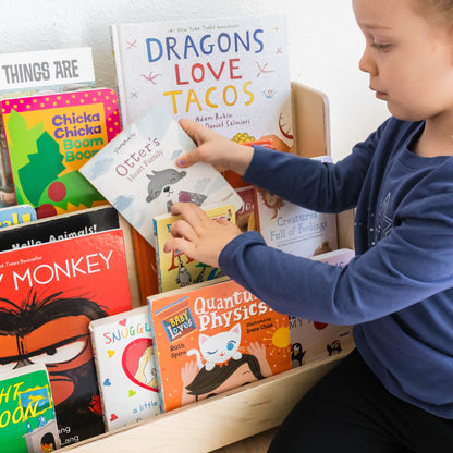 A young girl putting books into a floor bookshelf with front facing shelves. 
