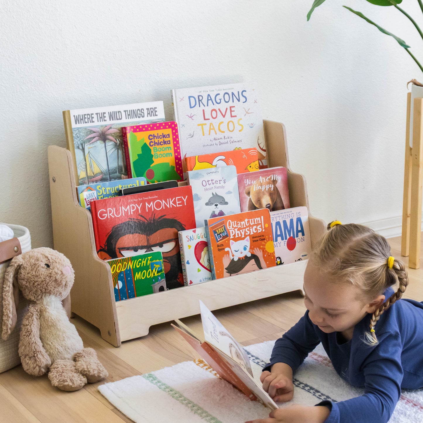 Girl reading a book next to a floor front facing bookshelf. 