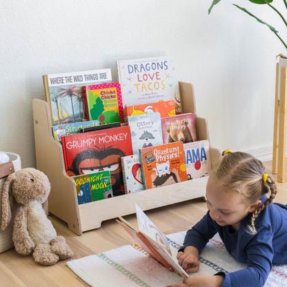 Girl reading a book next to a floor front facing bookshelf. 