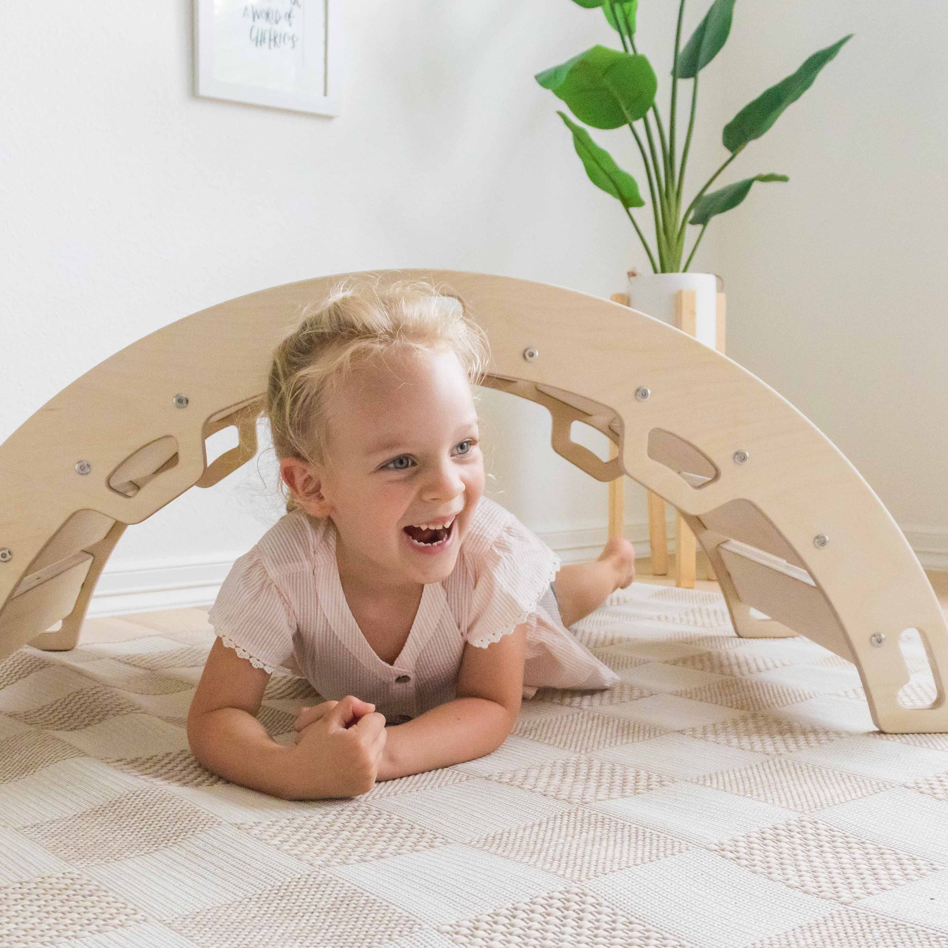 Child lying on a wooden arch toy in a home setting