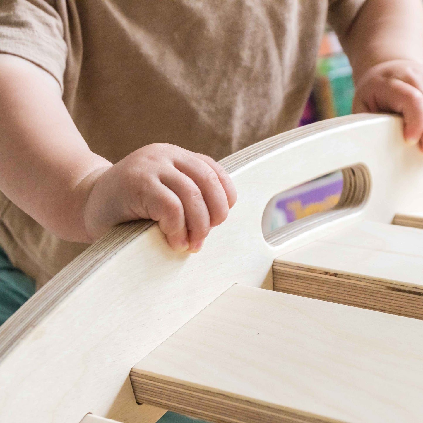 Child's hands holding onto a wooden montessori arch. 